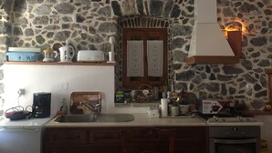 Eine Küche mit Steinwänden, einer Holztür und verschiedenen Geräten, darunter eine Kaffeemaschine, ein Toaster und ein Herd.