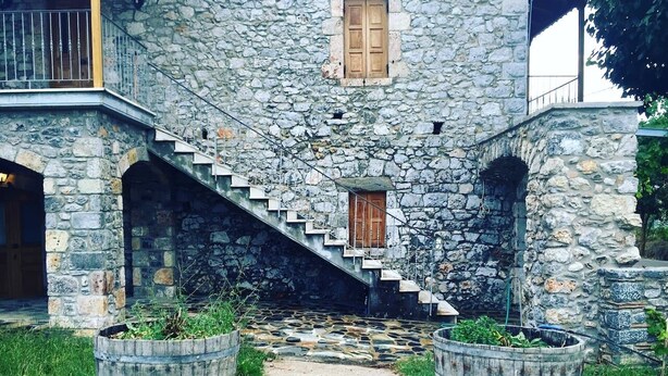 Ein Steinhaus mit einer Treppe, die zu einer Holztür führt. Vor dem Gebäude befinden sich zwei große Pflanzgefäße.