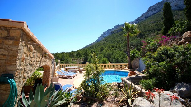 Un espace piscine doté de chaises longues, entouré de plantes et offrant une vue sur les montagnes en arrière-plan.