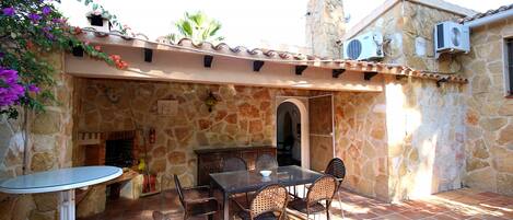 An outdoor patio with stone walls, a stone fireplace, a table with chairs, and air conditioning units.