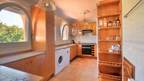 Une cuisine avec des meubles en bois, un lave-linge, un four à micro-ondes et un meuble à bouteilles.