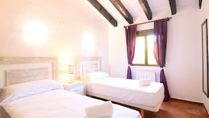 Une chambre avec deux lits simples, une table de chevet avec une lampe, une fenêtre avec des rideaux violets et un radiateur.