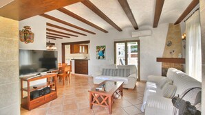 Uma sala de estar com televisão, mobiliário de madeira, área de jantar e cozinha.