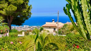 Uma vila costeira com vista para o mar, rodeada por vegetação exuberante e um céu claro.