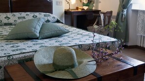 A neatly arranged bedroom with a patterned bedspread, a wooden bedside table with a hat, a lamp, and a vase with flowers. - RONDINE: Peaceful farmhouse close to Tuscany 's treasures, 1mile from shops far (Poggibonsi)