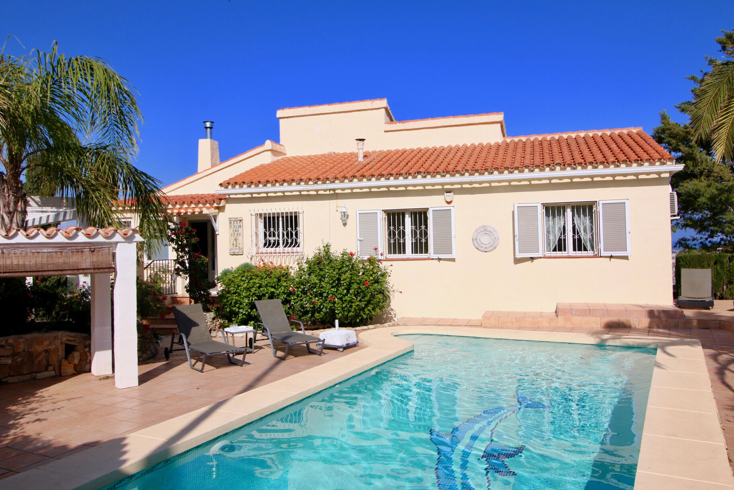 Une maison avec une piscine, une terrasse avec des chaises et un espace couvert comprenant une table et des chaises.