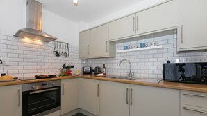 A modern kitchen with white cabinets, a stainless steel oven, a microwave, and a sink. - 21 Carthew Court - Garage Parking - Outside Space - Dog Friendly (St Ives)