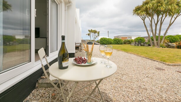 A table with a bottle of wine, a plate of grapes, and two glasses of wine on a gravel patio. - 21 Carthew Court - Garage Parking - Outside Space - Dog Friendly (St Ives)