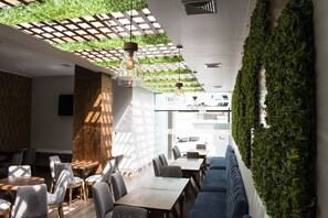 A modern restaurant interior with wooden tables and chairs, a blue sofa, and a green wall with plants. - Tecno Boutique Hotel (La Paz)