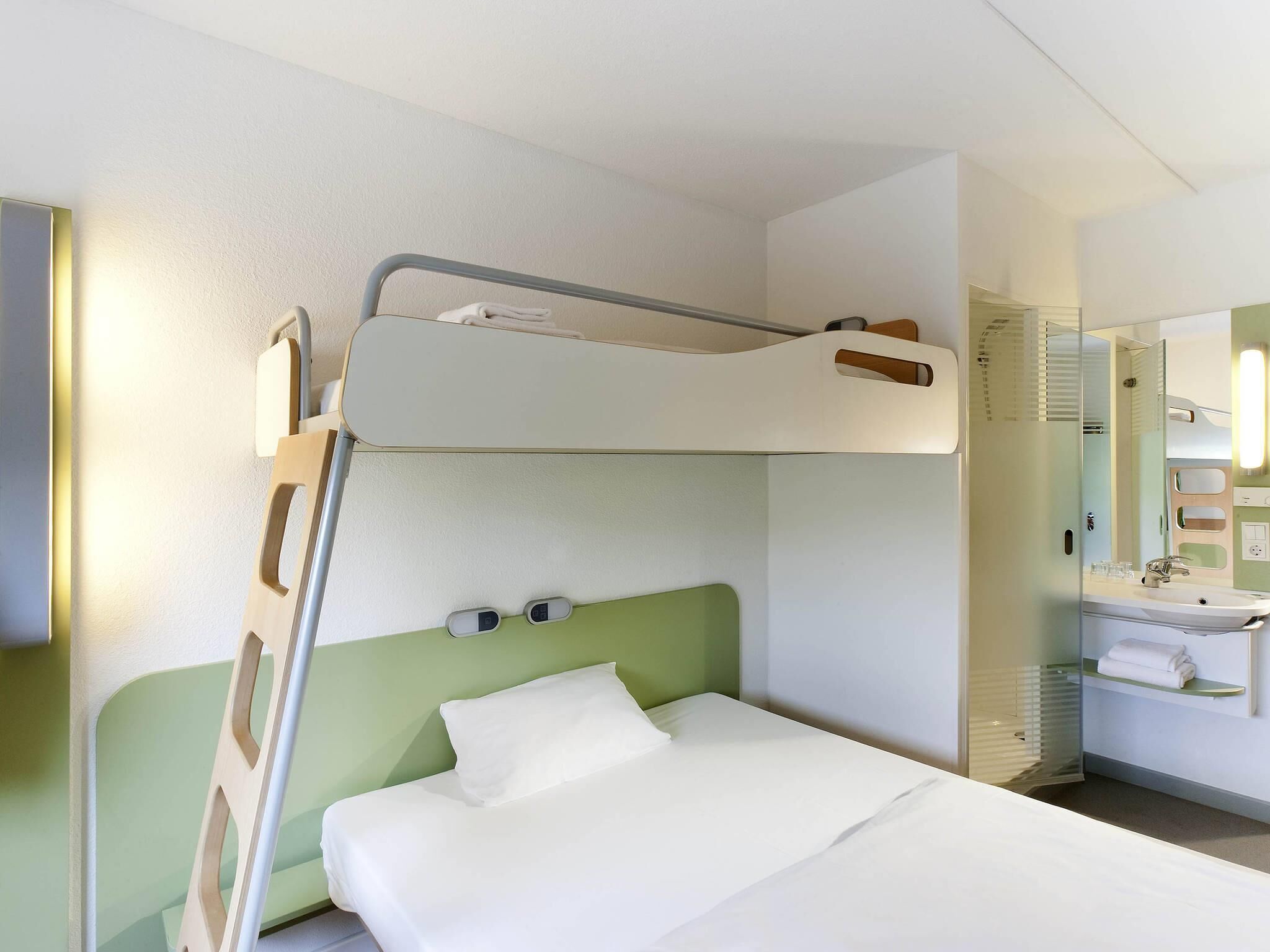 A bunk bed with a green headboard, a bedside table, and a mirror above the sink.