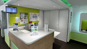 Un mostrador de recepción con techo iluminado en verde, un televisor montado y señales informativas.