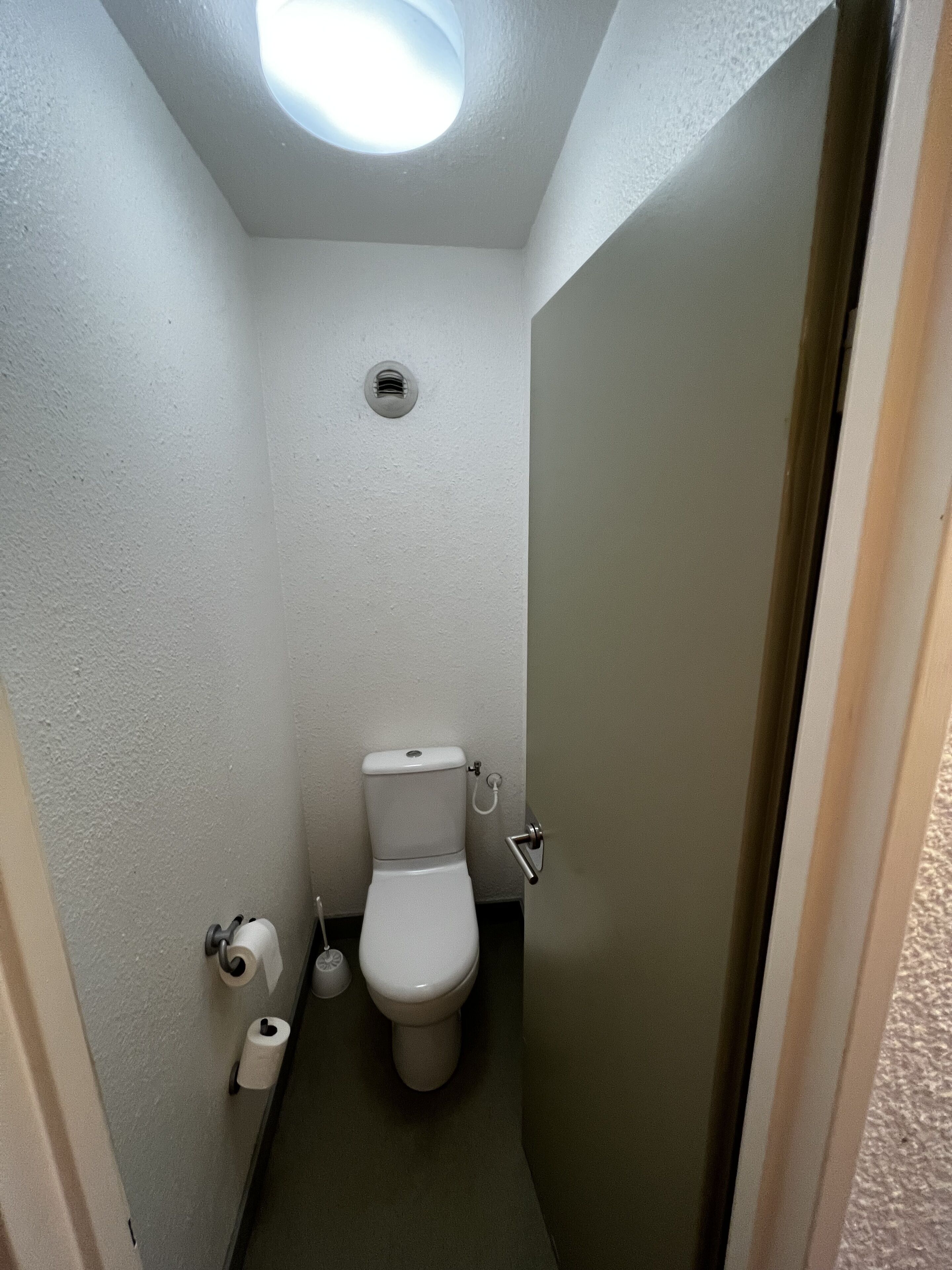 Un baño pequeño y estrecho con inodoro, dispensador de papel higiénico e iluminación en el techo.