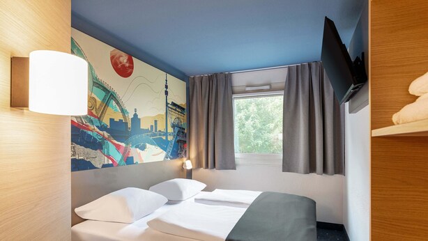 Habitación de hotel con cama, escritorio, televisor y ventana con cortinas.