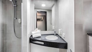 Un baño moderno con baldosas grises, un lavamanos con encimera negra, un cabezal de ducha manual y un perchero para toallas.