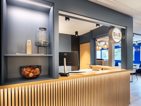 A reception desk with a modern design, a Dell monitor, a glass jar, and a fruit basket.