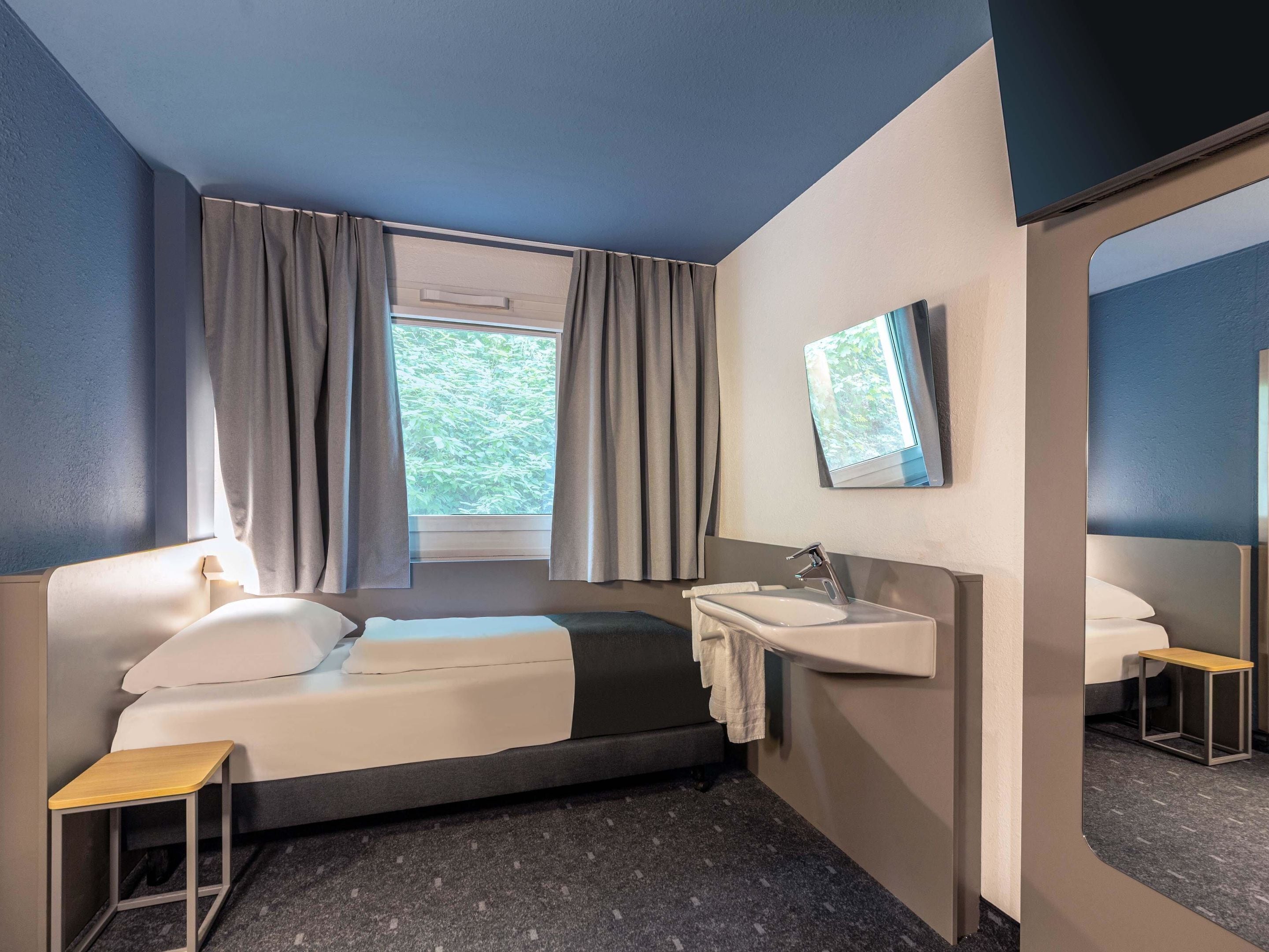 A modern hotel room with a bed, a bedside table, a sink, and a mirror.