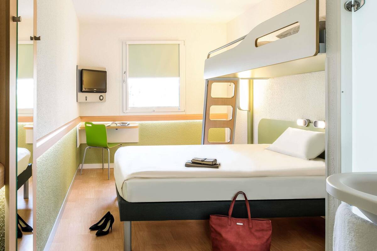 Una habitación de hotel con cama, escritorio, silla, televisor y baño.
