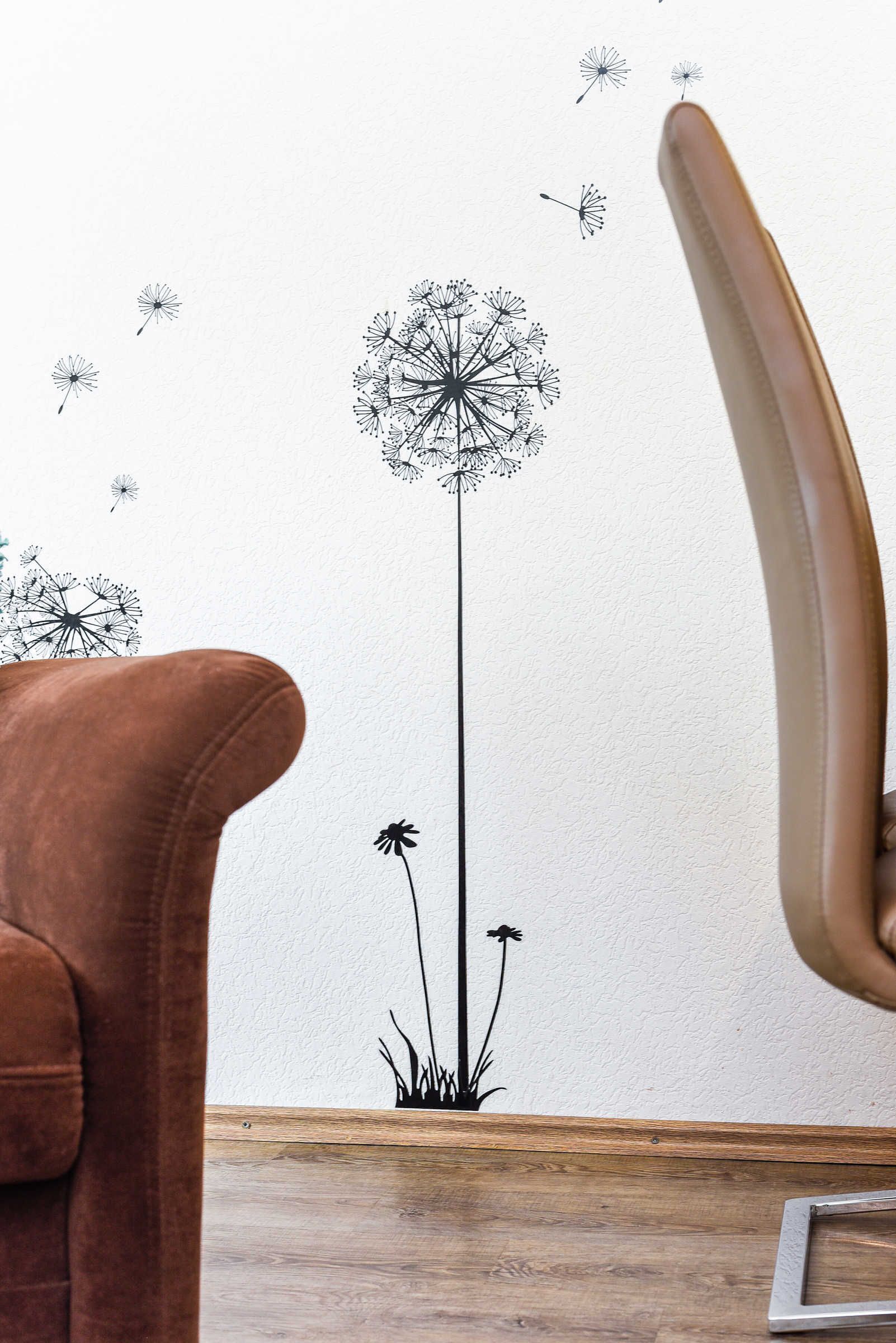 A room with a large wall decal of a dandelion, a brown leather chair, and a wooden floor.