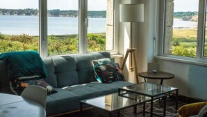 Une pièce avec vue sur un plan d’eau, un canapé avec des coussins, une table en verre et une lampe.