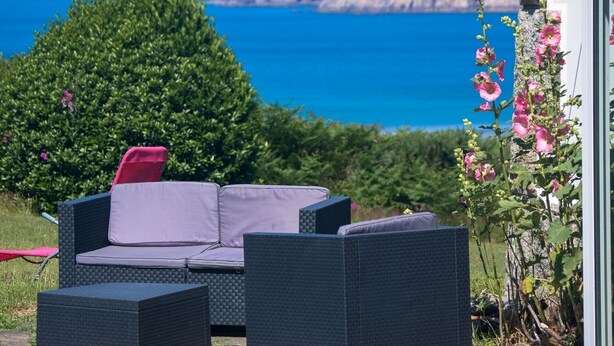 Une terrasse avec des meubles d’extérieur, une vue sur la mer et un jardin fleuri.