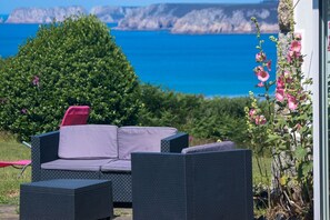 A patio with outdoor furniture, a view of the sea, and a garden with flowers. - House beach Goulien at 600m, breathtaking views of the ocean (crozon)