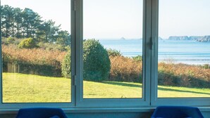 Une pièce avec deux chaises bleues et une grande fenêtre donnant sur un espace verdoyant et la mer.