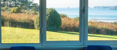 A room with two blue chairs and a large window offering a view of a grassy area and the sea.