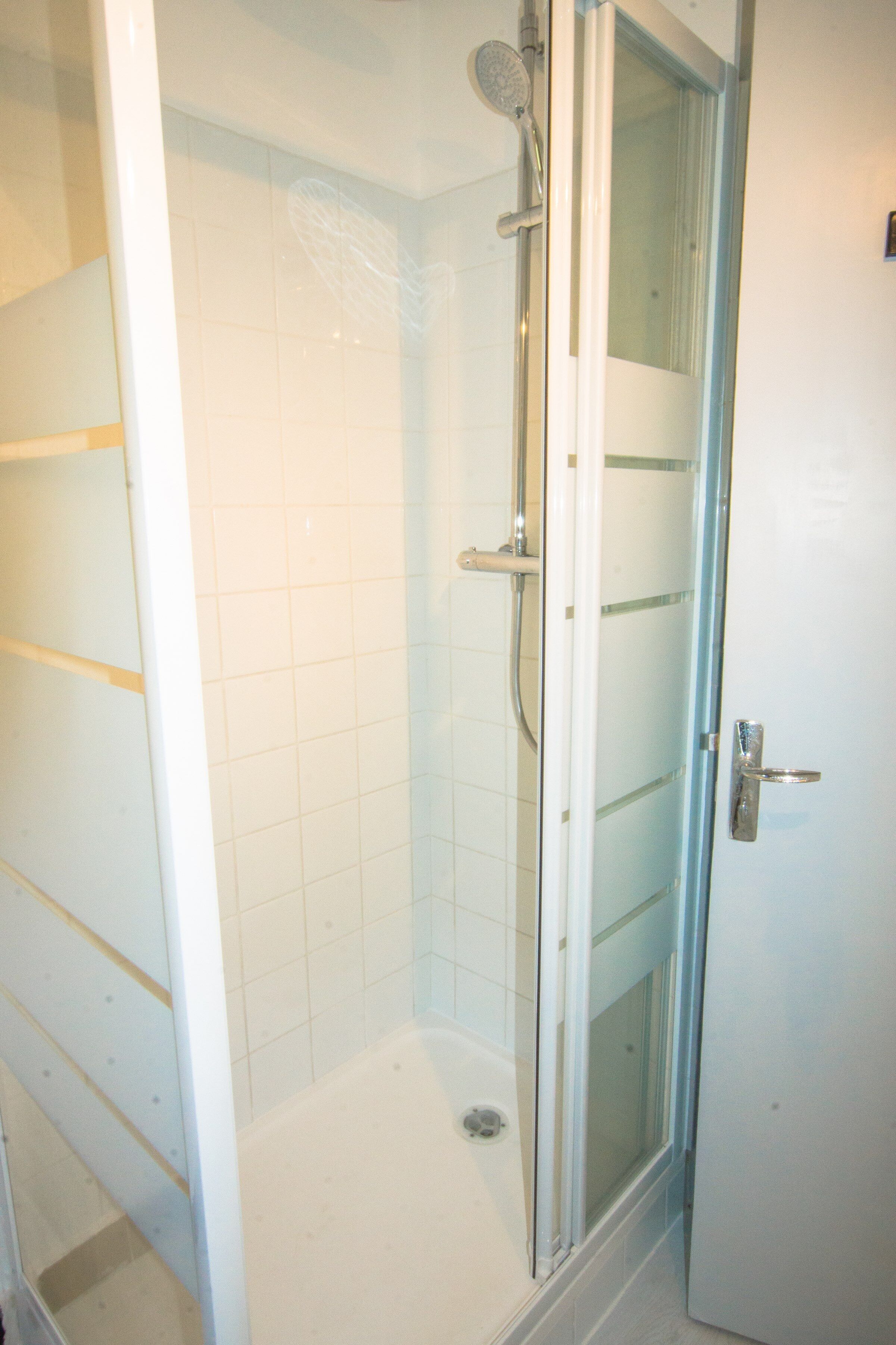 Un box de ducha con paredes de azulejos blancos, una ducha y una puerta con manija.