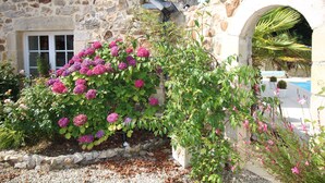Ein Steinhäuschen mit Fenster und einem Garten mit rosa Blüten.