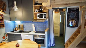 A compact kitchen with a microwave, stove, and wooden cabinets. A dining table with chairs is in the foreground. - Risoul - Apartment 04 - Fully equipped - WIFI - 30m² - Foot of ski area (Risoul 1850)