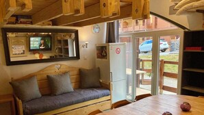 A cozy room with a wooden sofa, a small table, and a refrigerator. - Risoul - Apartment 04 - Fully equipped - WIFI - 30m² - Foot of ski area (Risoul 1850)