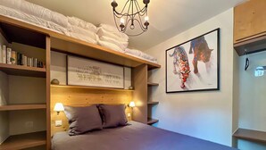 Een slaapkamer met een stapelbed, een nachtkastje met een lamp, een raam met een citaat en kleurrijke kunst aan de muur.