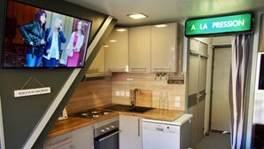 A compact kitchen with a stove, sink, and dishwasher, a dining table with chairs, and a TV mounted on the wall. - Risoul - Duplex 66 - Fully equipped - WIFI - 60m² - Foot of ski slopes (Risoul 1850)