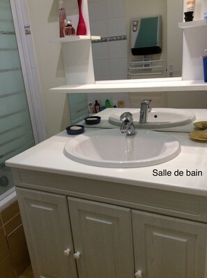 A bathroom with two sinks, a mirror, and a shelf with toiletries. - Apartment in townhouse (Embrun)