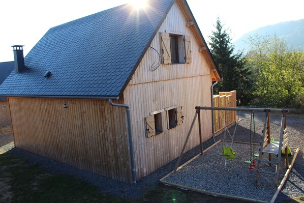 A wooden house with a sloped roof, a small porch, and a swing set. - Chalet "le pradou" free wifi, heating included (Murol)