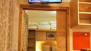 A cozy room with a bed, a small table, and a television mounted on the wall. - Risoul - Apart 202 - Pool/Sauna - WIFI - Fully equipped - Foot of slopes (Risoul)