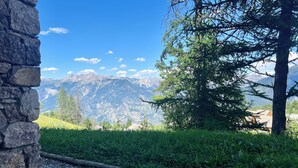 Un mur de pierres, un chemin de gravier et une vue sur les montagnes et les arbres.