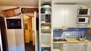 A compact kitchen with white cabinets, a microwave, a stove, and a wooden table. - Risoul - Studio 02 - Fully equipped - WIFI - 30m² - Foot of ski area (Risoul 1850)