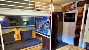 A compact room with a bunk bed, a small sofa, a wooden table, and a refrigerator. - Risoul - Studio 02 - Fully equipped - WIFI - 30m² - Foot of ski area (Risoul 1850)