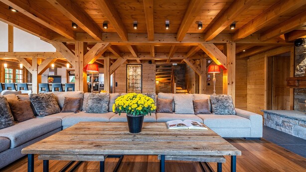 Un intérieur chaleureux avec un plafond en bois, un ensemble de canapés, une table basse et un vase rempli de fleurs jaunes.
