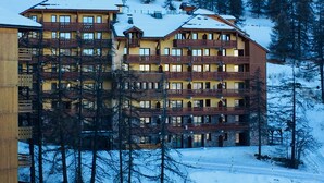 A multi-story hotel with balconies, surrounded by snow-covered trees and a mountainous backdrop. - Risoul - Apart 410 - Pool/Sauna - WIFI - Fully equipped - Foot of slopes (Risoul)