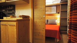 A compact room with a kitchenette, a bed with a red blanket, and a wooden wardrobe. - Risoul - Apart 410 - Pool/Sauna - WIFI - Fully equipped - Foot of slopes (Risoul)