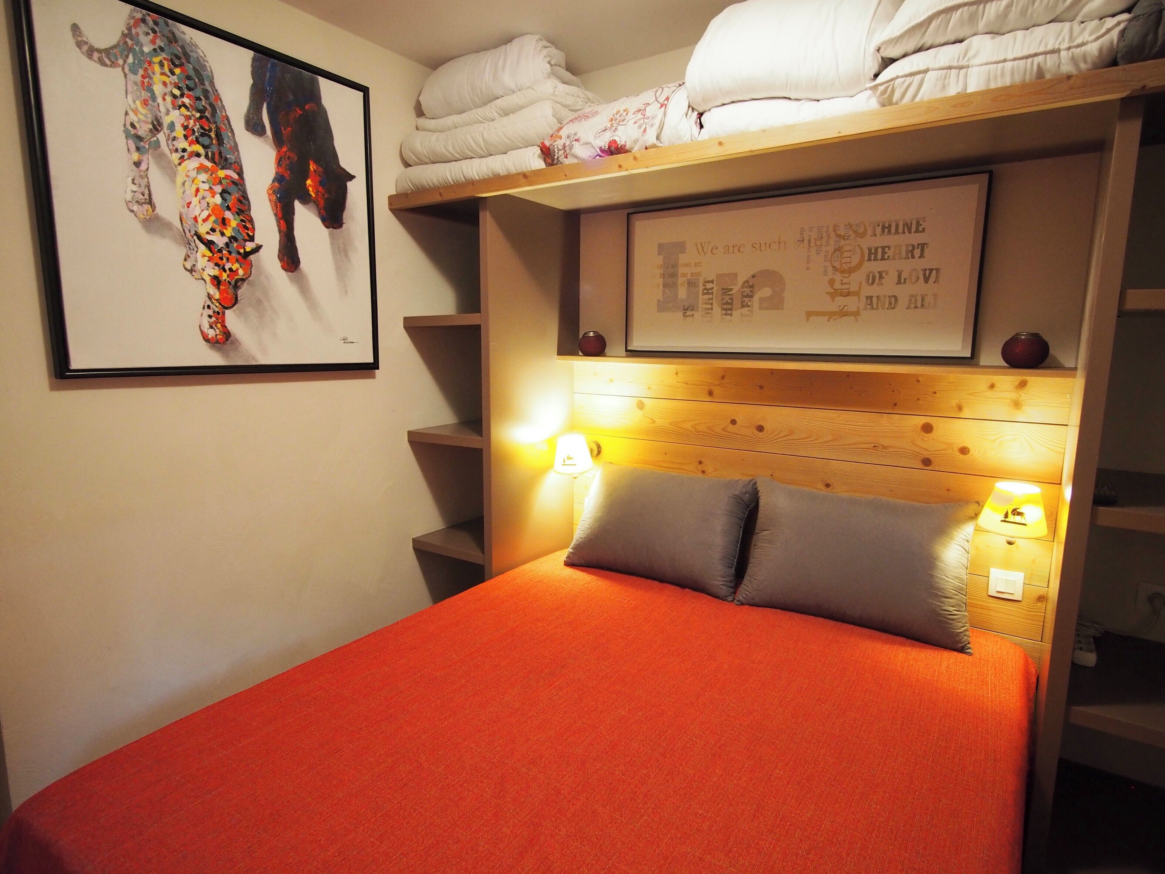 Een slaapkamer met een bed, een hoofdbord met wandlampen, een citaat in een lijst en een schilderij van katten.