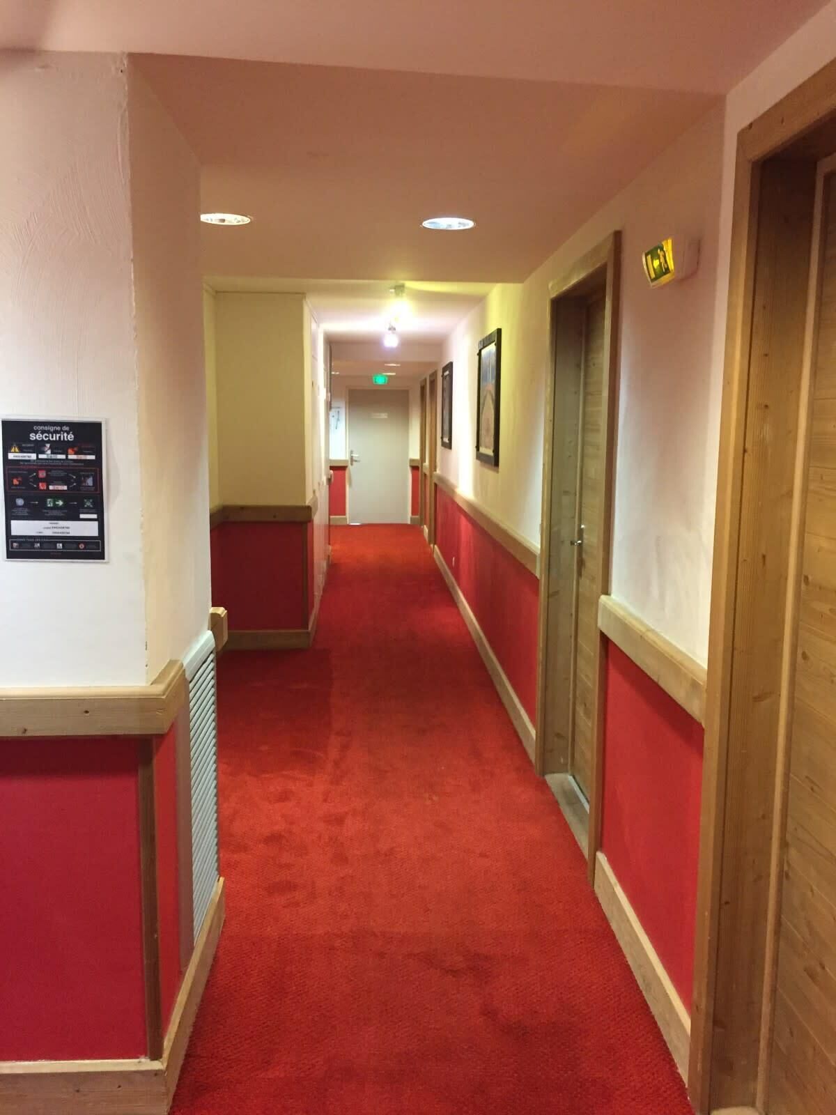 Um corredor com carpete vermelho, portas de madeira e uma placa de segurança na parede.