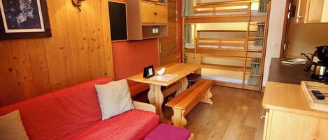 A cozy room with a red sofa, wooden benches, a table, and a bunk bed.