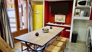 A dining area with a wooden table, four benches, a TV mounted on the wall, and a microwave on a shelf. - Risoul - Studio 08 - Fully equipped - WIFI - 30m² - Foot of ski area (Risoul 1850)