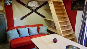 A room with a red sofa, a wooden table, and a wooden ladder. - Risoul - Studio 08 - Fully equipped - WIFI - 30m² - Foot of ski area (Risoul 1850)