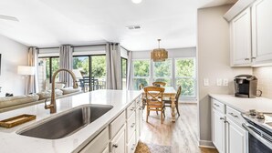 A modern kitchen with a central island, white cabinetry, and a dining area with a wooden table and chairs. - Pool View, Open Plan, Pet Friendly & No Carpeting! (Hilton Head Island)