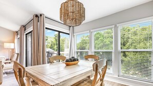 A dining area with a wooden table, four chairs, a chandelier, and large windows with blinds. - Pool View, Open Plan, Pet Friendly & No Carpeting! (Hilton Head Island)