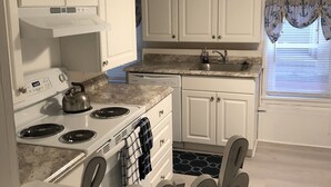 Una cocina con gabinetes blancos, estufa y pileta.